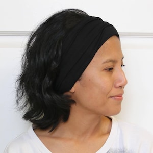 Pode incluir: Uma faixa de cabelo preta de tecido usada por uma pessoa com cabelo curto e escuro. A faixa é dobrada e tem um design simples.