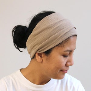 Pode incluir: Uma faixa de cabeça de tecido marrom claro usada na cabeça de uma pessoa. A faixa de cabeça é dobrada e tem um design simples.