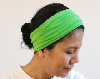 May include: A bright lime green headband made of a smooth, flexible fabric. The accessory features a wide, gathered design that wraps around the head, creating soft horizontal folds across the surface of the material for a textured appearance.