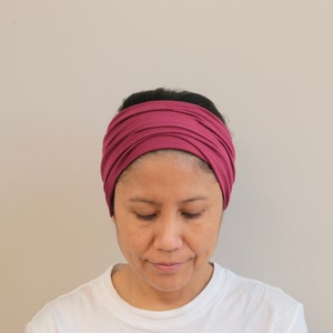 Pu&ograve; includere: Una donna indossa una fascia per capelli color borgogna. La fascia &egrave; realizzata in un tessuto morbido ed elastico ed &egrave; annodata sulla parte superiore della testa.