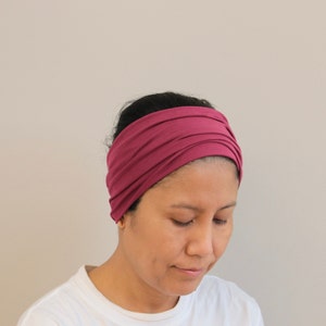 Pu&ograve; includere: Una donna indossa una fascia per capelli a turbante color borgogna. La fascia &egrave; realizzata in tessuto morbido ed elastico ed &egrave; progettata per essere indossata comodamente.