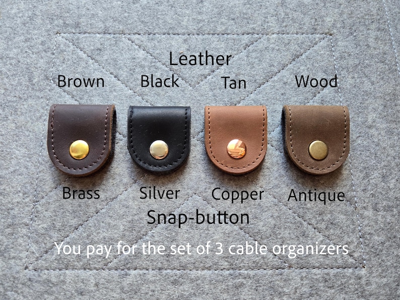May include: Four leather cable organizers in brown, black, tan, and wood colors, each featuring a metal snap-button in brass, silver, copper, or antique finishes. Text labels identify the leather colors and metal snap-button finishes.