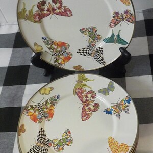 May include: A set of decorative plates with a butterfly design. The plates have a white background adorned with colourful butterfly patterns in orange, red, and black. Each plate has a gold rim, adding a touch of elegance.