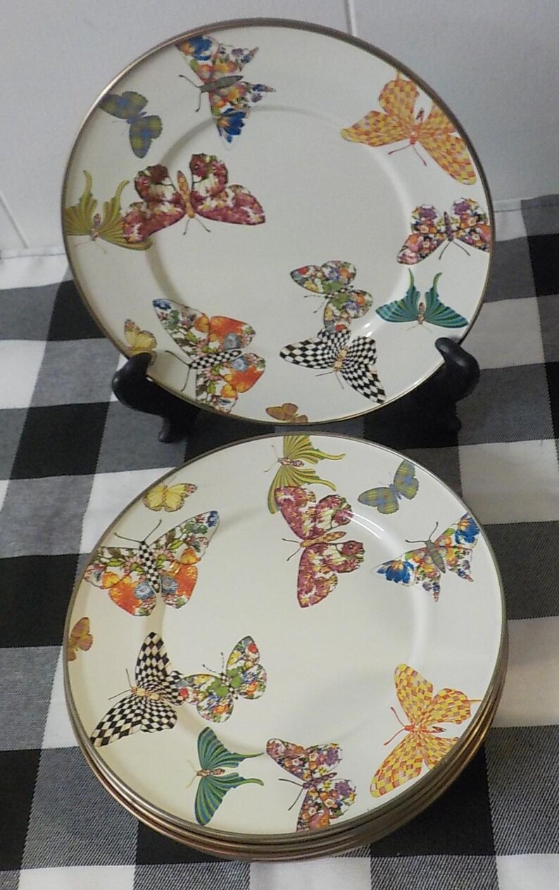 May include: A set of decorative plates with a butterfly design. The plates have a white background adorned with colourful butterfly patterns in orange, red, and black. Each plate has a gold rim, adding a touch of elegance.