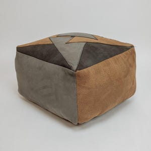 Op de afbeelding: Een vierkante patchwork poef in tinten bruin, grijs en beige. De bovenkant heeft geometrische vormen, terwijl de zijkanten effen kleuren hebben. Dit decoratieve accentstuk voegt een vleugje moderne stijl toe aan elke woonruimte.
