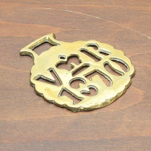 Peut inclure: Un objet en laiton doré, probablement un ornement de cheval, avec un motif ajouré. Il présente les lettres "VR" et "GR" entrelacées, des bords festonnés et une boucle pour l'accrocher. L'ensemble est de couleur dorée.