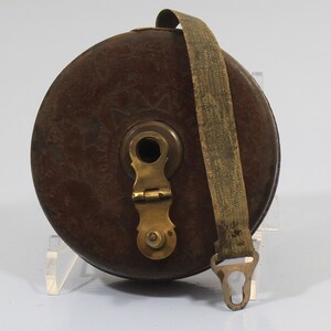 May include: A vintage wooden tape measure with a brass winding mechanism and a leather strap. The tape measure is brown and has a worn, antique look.