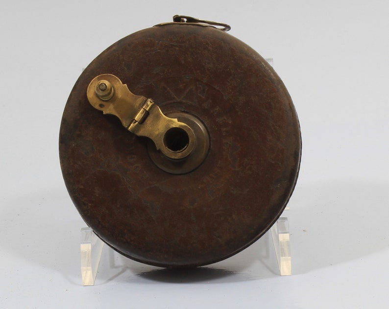 May include: A vintage wooden tape measure with a brass winding mechanism and a leather case. The case is brown and has a worn look. The brass mechanism has a small handle and a hole in the center.
