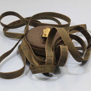 May include: A vintage wooden tape measure with a brown leather case and a brass end cap. The tape is coiled and has a printed scale in inches.
