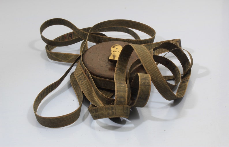 May include: A vintage wooden tape measure with a brown leather case and a brass end cap. The tape is coiled and has a printed scale in inches.
