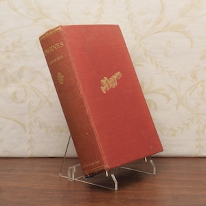 Puede incluir: Un libro antiguo titulado "Engines" de Andrade, con una cubierta roja y letras doradas. El libro se exhibe en un soporte de acrílico transparente, sobre un fondo estampado.