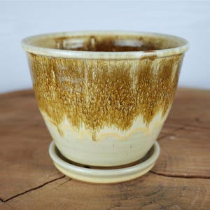 May include: A ceramic plant pot with a matching saucer, featuring a cream-colored base and a textured, dripping brown glaze that cascades from the rim toward the center, creating a distinct two-tone appearance with a smooth, glossy finish.