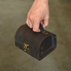 Peut inclure: Une bo&icirc;te en cuir marron avec un fermoir en laiton et une poign&eacute;e. La bo&icirc;te a une surface textur&eacute;e et est ferm&eacute;e.