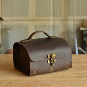 Peut inclure: Une sacoche en cuir marron avec une fermeture en laiton et une poign&eacute;e sup&eacute;rieure. Le sac a une forme rectangulaire et est d&eacute;cor&eacute; de clous en laiton.