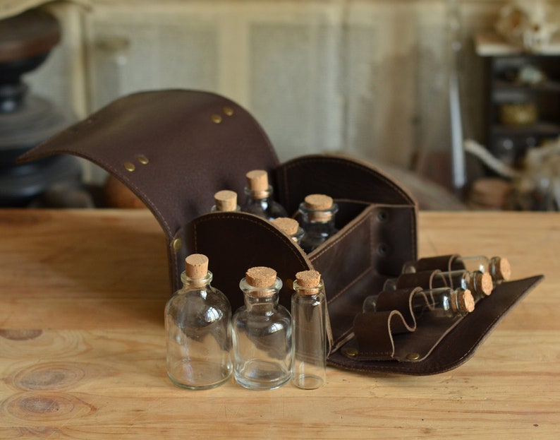 Peut inclure: Une bo&icirc;te de voyage en cuir marron avec un couvercle &agrave; charni&egrave;res, ouverte pour r&eacute;v&eacute;ler plusieurs petites bouteilles en verre avec des bouchons en li&egrave;ge. Les bouteilles sont dispos&eacute;es en rang&eacute;es &agrave; l'int&eacute;rieur de la bo&icirc;te.