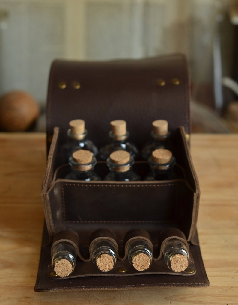Peut inclure: Une bo&icirc;te de transport en cuir marron avec un rabat qui s'ouvre pour r&eacute;v&eacute;ler six petites bouteilles en verre avec des bouchons en li&egrave;ge. La bo&icirc;te a une sangle avec six fentes suppl&eacute;mentaires pour les bouteilles.