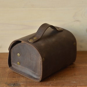 Peut inclure: Un sac en cuir brun avec une poign&eacute;e sup&eacute;rieure et des accents en laiton. Le sac a une forme arrondie et est fait de cuir vieilli.