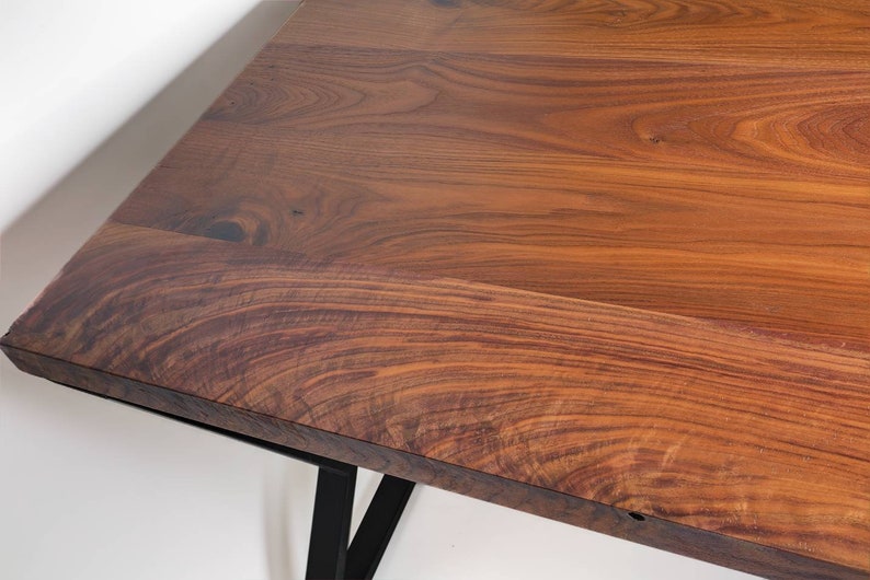 May include: Close-up of a wooden table with a rich, warm brown color. The table has a natural wood grain pattern and is supported by black metal legs. The table's surface is smooth and appears to be well-finished.