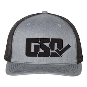 Könnte beinhalten: Graue Trucker-Cap mit schwarzem Mesh-Rücken und gebogenem Schirm. Auf der Vorderseite sind die schwarzen Buchstaben "GSD" in einem schwarzen Rechteck mit einem Häkchen-Symbol abgebildet.