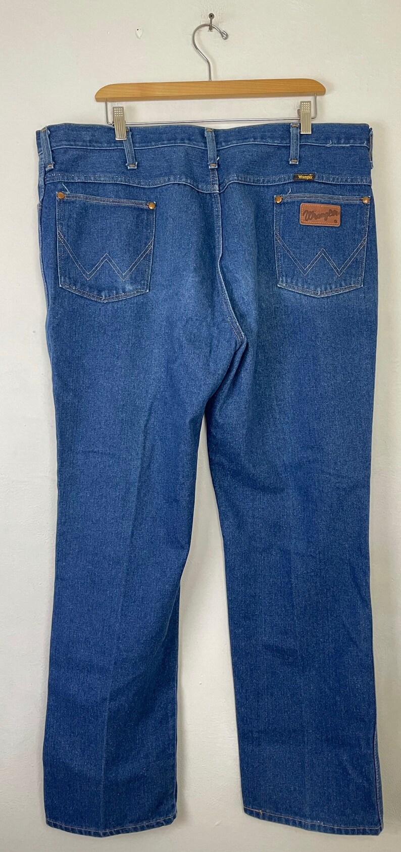 Może przedstawiać: Dżinsy z niebieskiego denimu z brązową sk&oacute;rzaną naszywką na tylnej kieszeni z napisem "Wrangler".