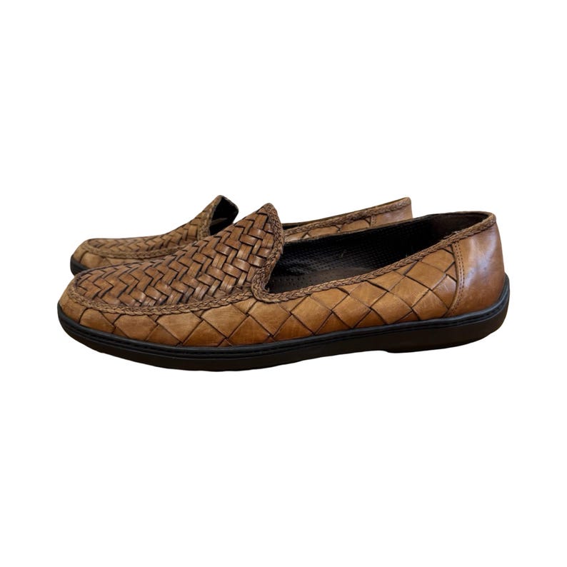 May include: A pair of brown leather loafers with a woven design. The shoes have a slip-on style with a rounded toe and a black sole. The leather has a distressed look.