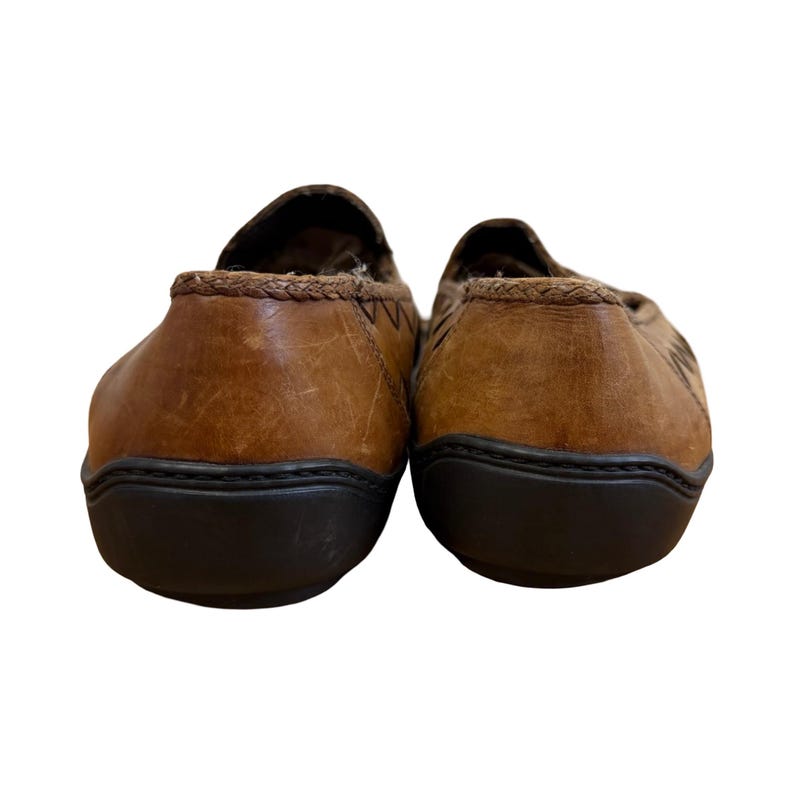 May include: A pair of brown leather slip-on shoes. The shoes have a dark brown sole and a stitched design on the back. The interior lining is a patterned fabric.