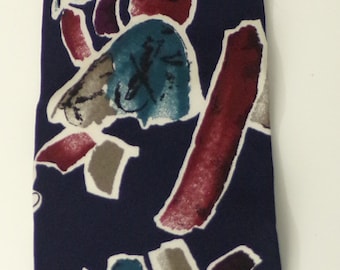May include: A navy blue silk tie with a colorful abstract pattern. The pattern features various shapes and colors, including teal, red, purple, and gray.