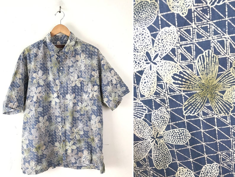 Puede incluir: Una camisa azul de manga corta con botones y un estampado floral blanco y verde. La camisa tiene un patr&oacute;n geom&eacute;trico en el fondo.