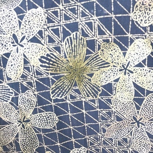 Puede incluir: Una tela negra con un patr&oacute;n repetitivo de flores doradas y formas geom&eacute;tricas. Las flores tienen un dise&ntilde;o punteado y en espiral.