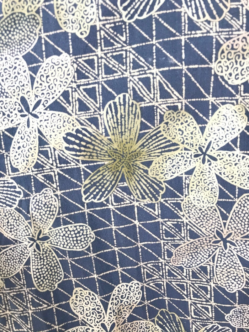 Puede incluir: Una tela negra con un patr&oacute;n repetitivo de flores doradas y formas geom&eacute;tricas. Las flores tienen un dise&ntilde;o punteado y en espiral.