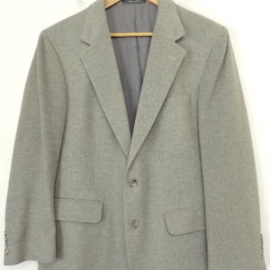 Puede incluir: Una chaqueta gris con cierre de dos botones y un bolsillo único en el lado izquierdo.