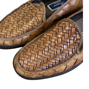 May include: Close-up of two brown woven leather loafers. The shoes have a basket weave design on the top and sides. The soles are black, and the shoes appear to be unworn.