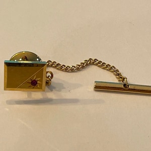 May include: Gold tie tack with a red stone in the centre and a chain attached to a gold bar.