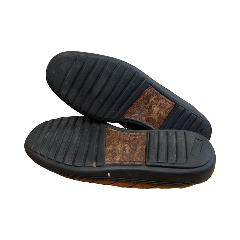 May include: A pair of brown leather loafers with black rubber soles. The soles have a textured, ridged design for grip. The leather uppers are visible, showing a quilted pattern. The shoes are shown from the bottom.