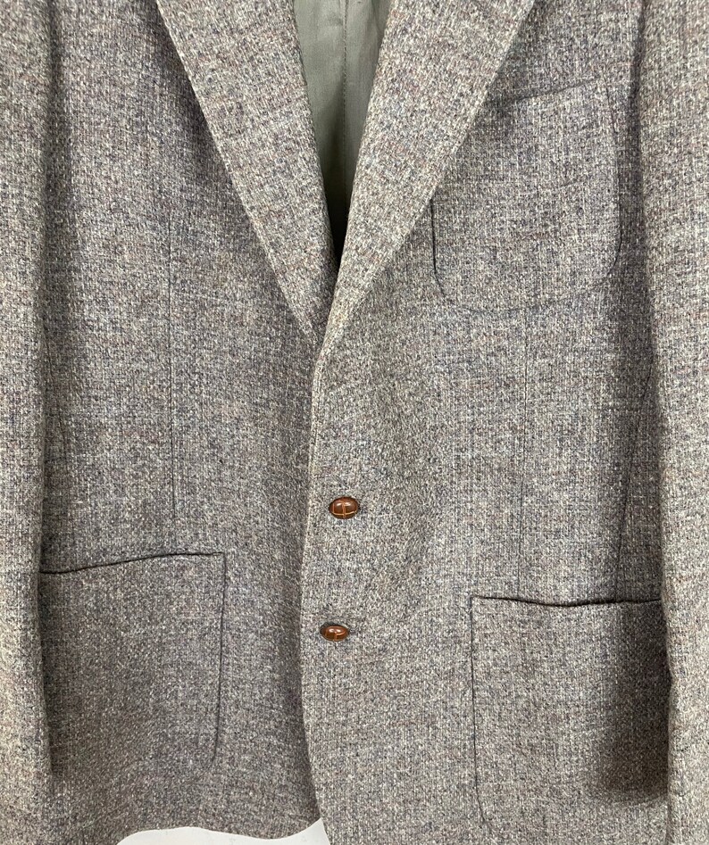 May include: A gray tweed blazer with two brown buttons and two flap pockets.