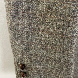 May include: Close-up of the brown tweed fabric of a jacket with two brown buttons.