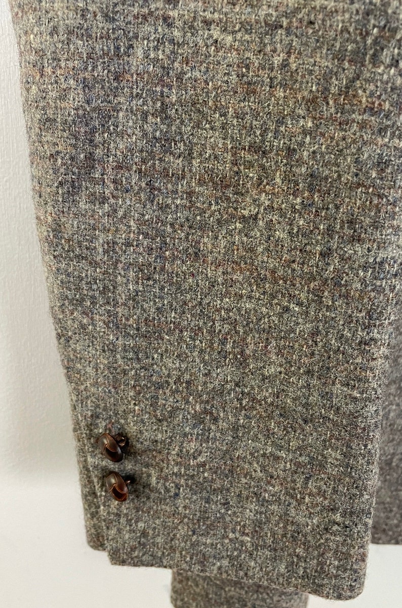 May include: Close-up of the brown tweed fabric of a jacket with two brown buttons.