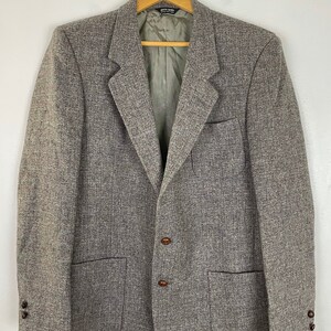 May include: A gray tweed blazer with brown buttons and two flap pockets. The blazer has a single-breasted closure and a notched lapel.
