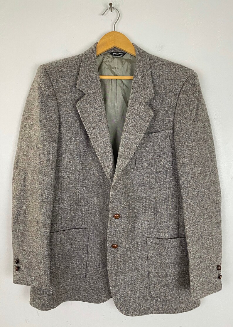 May include: A gray tweed blazer with brown buttons and two flap pockets. The blazer has a single-breasted closure and a notched lapel.