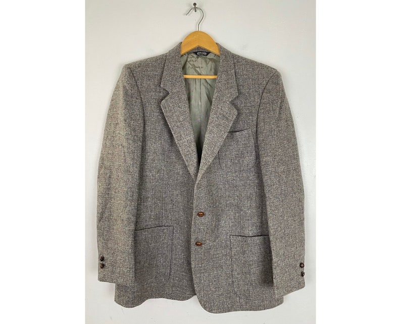 May include: A gray tweed blazer with two button closures and two flap pockets. The blazer has a brown lining and brown buttons.