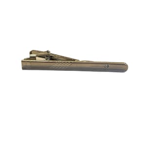 May include: A silver tie clip with a textured design. The clip has a spring mechanism and a small hole on the top.