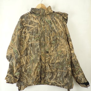 May include: A camouflage jacket with a zipper closure and a hood. The jacket has a brown, green, and tan pattern with a leafy design.