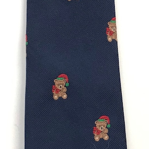 Puede incluir: Una corbata azul marino con un patrón repetido de osos de peluche marrones que llevan gorros de Papá Noel rojos y ribetes verdes.