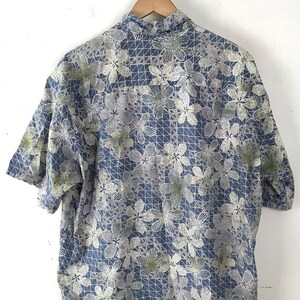 Puede incluir: Una camisa azul de manga corta con un estampado floral blanco y verde. La camisa tiene un cuello abotonado y un corte holgado.