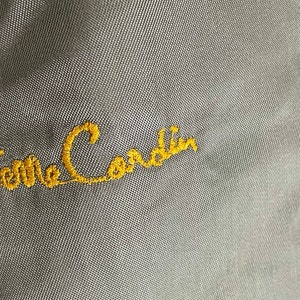 May include: A close-up of a gray fabric with the embroidered text "Pierre Cardin" in yellow thread.