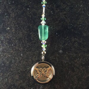 Może przedstawiać: Srebrny medalion z motywem motyla wiszący na koralikowym łańcuszku z zielonymi i przezroczystymi kryształami i białym piórem.