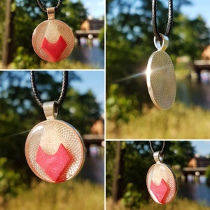 Può includere: Una collana con un ciondolo d'argento e un ciondolo rotondo in resina trasparente. Il ciondolo contiene una forma geometrica rosa all'interno. La collana è su un cordoncino nero.