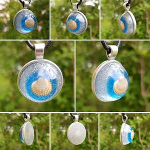 Könnte beinhalten: Eine silberne Halskette mit einem runden blauen und weißen Glasanhänger, der eine Muschel zeigt. Der Anhänger hat eine glitzernde Oberfläche.