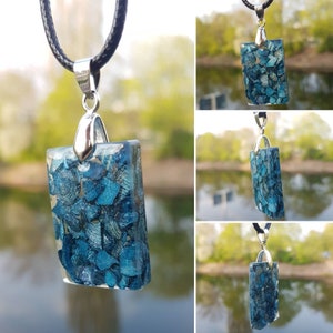 Könnte beinhalten: Eine silberne Kettenkette mit einem rechteckigen Anhänger mit einem blauen und silbernen Harzdesign. Der Anhänger ist mit kleinen, schillernden Materialstücken gefüllt.