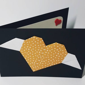 Schwarze Klappkarte mit orangem Origami-Herz mit weißen Flügeln
